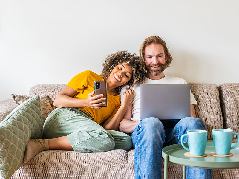 TrutzContent - keine Chance für Werbeblocker Ein fröhliches Paar mit Smartphone und Laptop auf dem Sofa